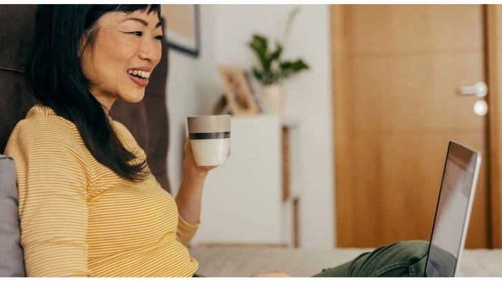 Smiling woman holding mug working on laptop computer