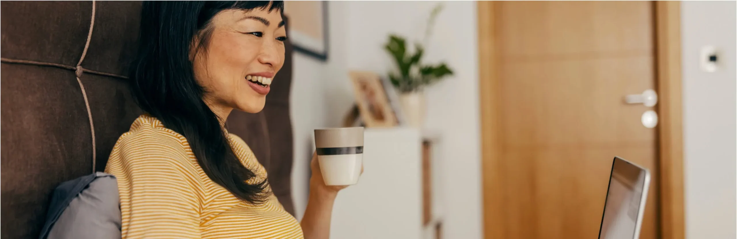 Smiling woman holding mug working on laptop computer