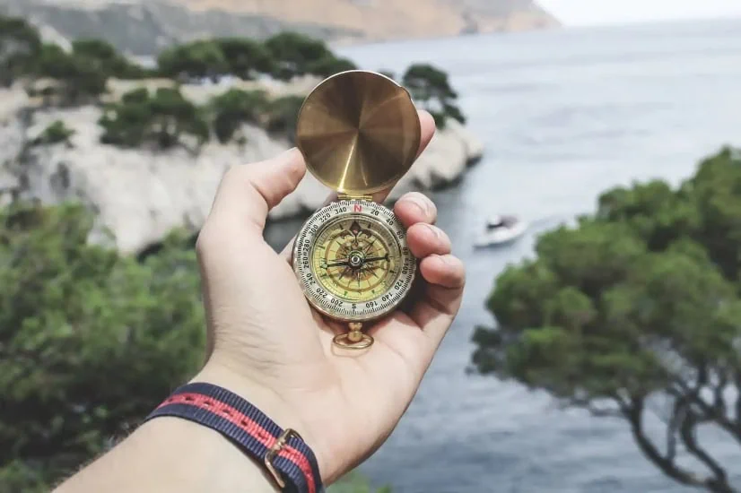 Hand holding a compass above a large body of water